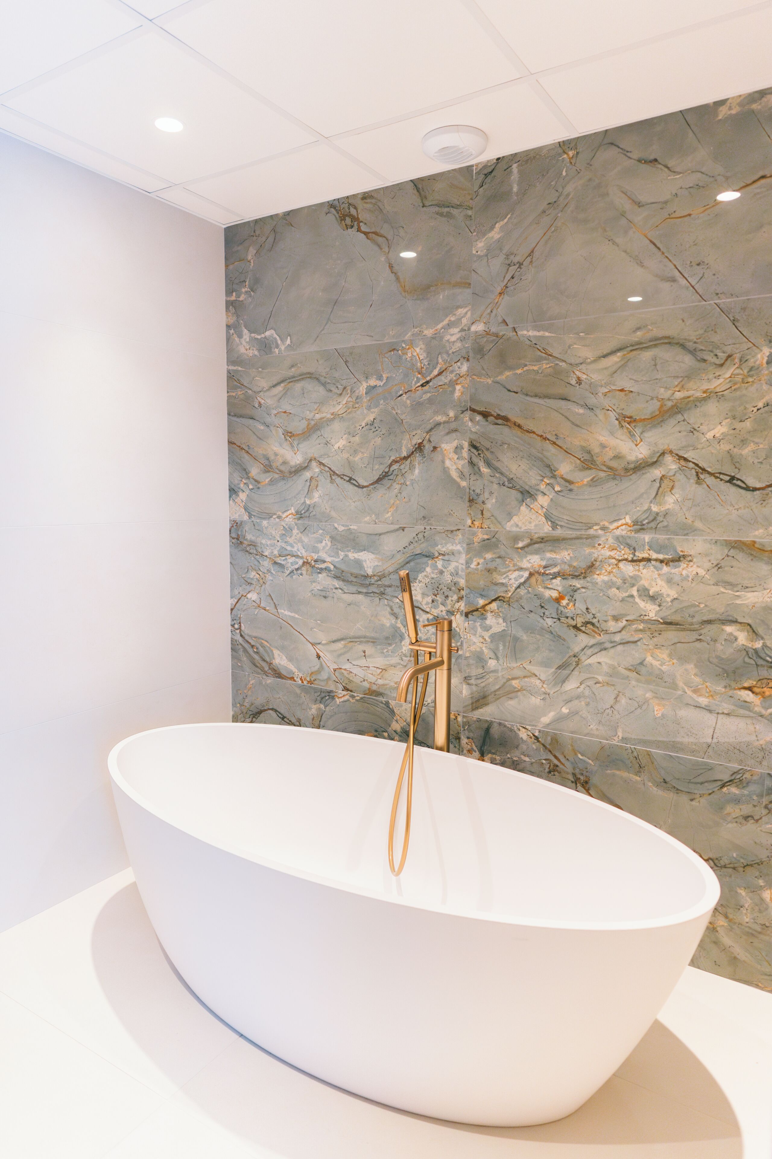 A modern bathroom with a freestanding bathtub, marble wall, and a gold faucet.
