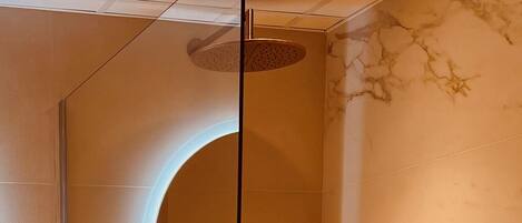 A modern bathroom with a glass-enclosed shower, marble walls, and a round mirror.