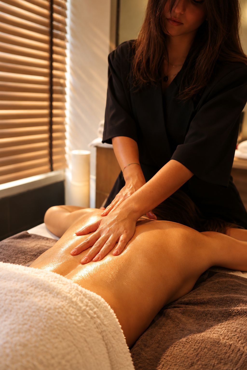 Une personne reçoit un massage sur une table de massage, une serviette est à portée de main et, à l'arrière-plan, on aperçoit une fenêtre avec des stores.