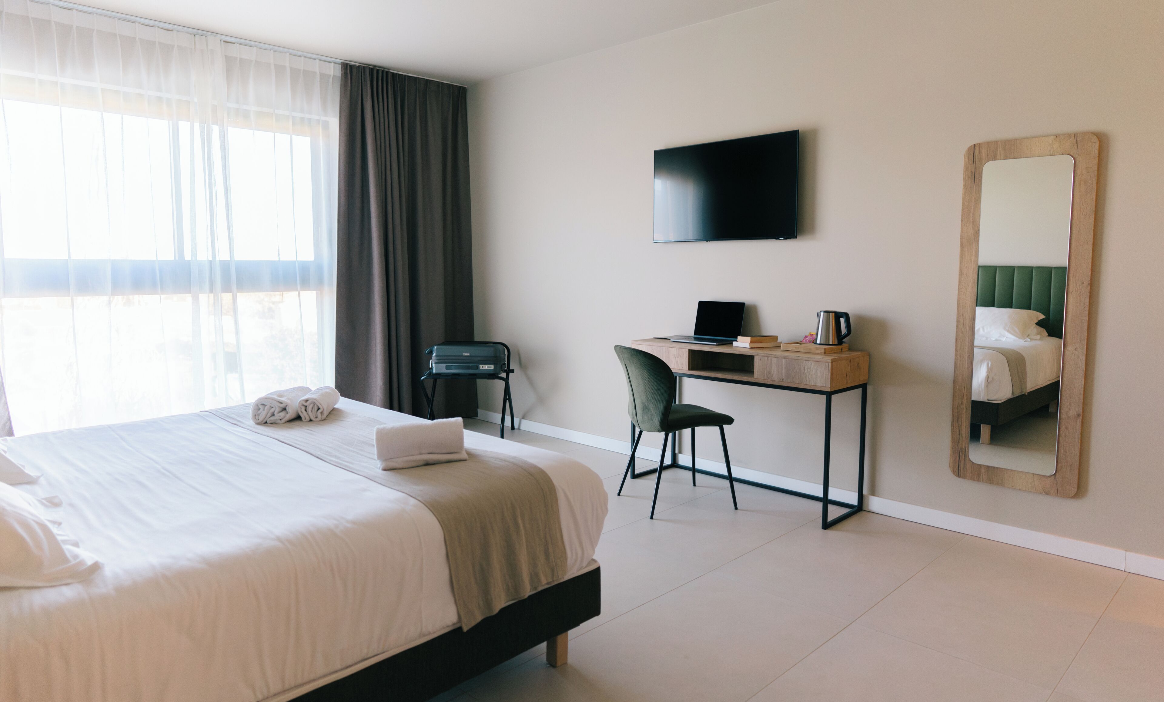 Habitación de hotel con cama, escritorio con computadora portátil, silla, televisor y un espejo grande.