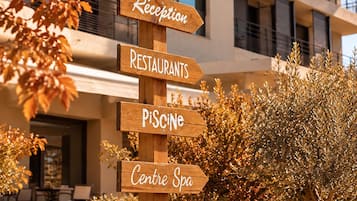 A wooden signpost with directional arrows pointing to amenities such as a reception, restaurants, a spa, and a pool.