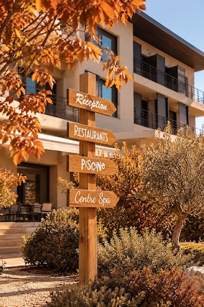 Un panneau indicateur en bois, muni de flèches directionnelles, indique l’emplacement des différents services proposés, tels qu’une réception, des restaurants, un spa et une piscine.