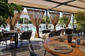 Een buitenterras met tafels en stoelen, een zwembad op de achtergrond en uitzicht op zee.