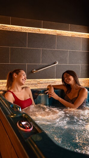 Deux personnes dans un jacuzzi, avec un mur en pierre et une rambarde métallique en arrière-plan.