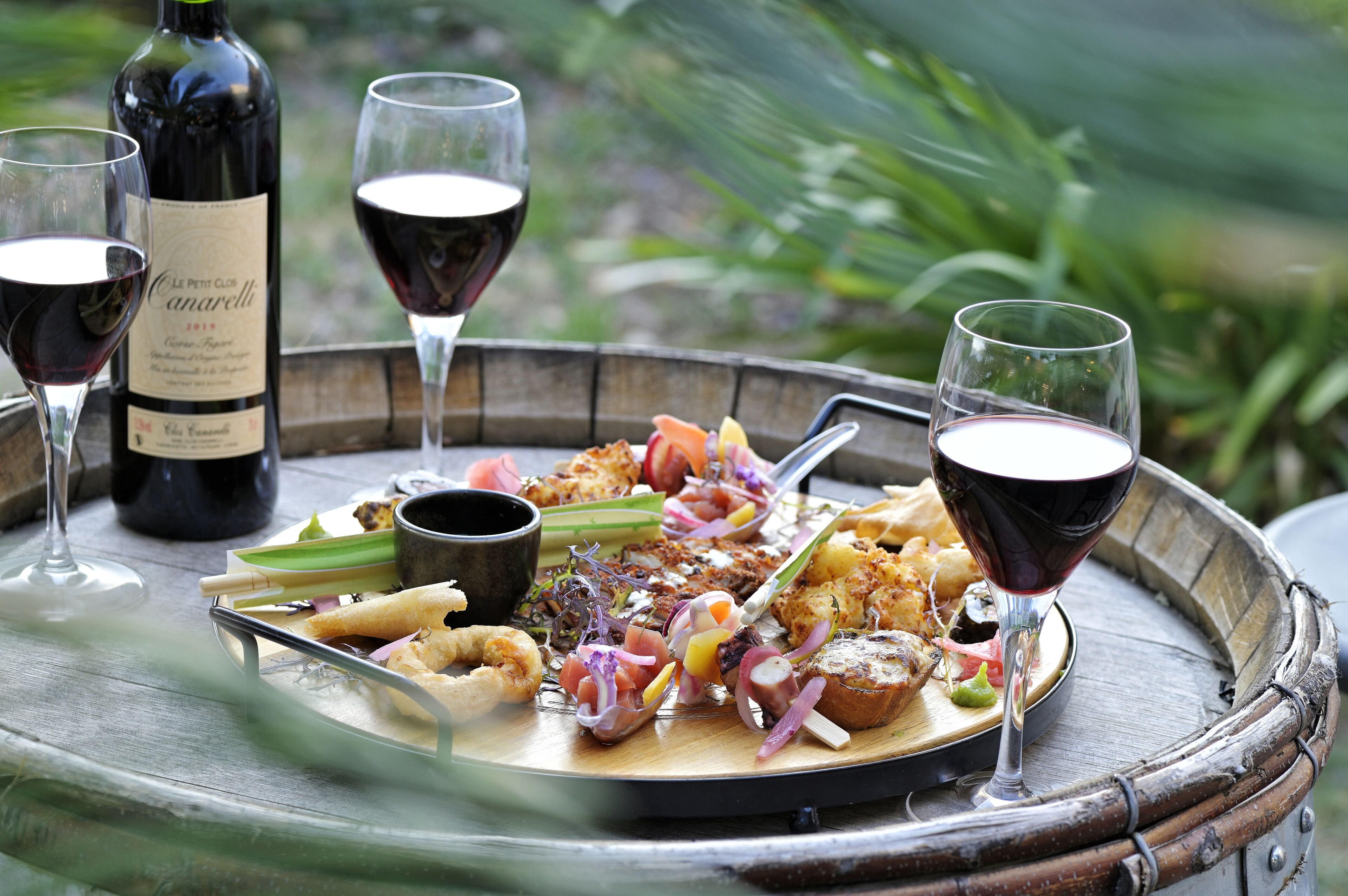 A wooden tray with a variety of seafood and vegetables, accompanied by wine glasses and a bottle of wine.