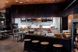 A restaurant with a bar area, wooden stools, and shelves stocked with condiments and beverages.