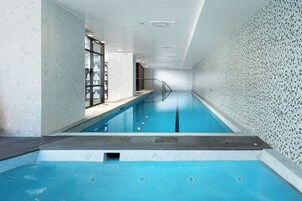 Piscina interna con parete piastrellata, solarium in legno e porta in vetro che dà su un'altra zona.