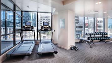 A gym with treadmills, dumbbells, and a view of the city through large windows.