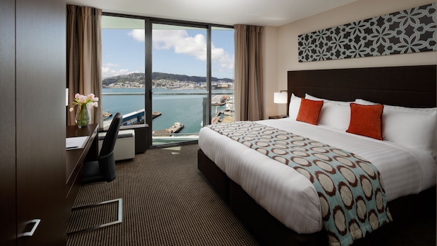 A hotel room with a large bed, a desk, and a view of a body of water. - Rydges Wellington (Wellington)