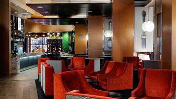 A modern lobby with red upholstered chairs, a bar area, and a green wall.