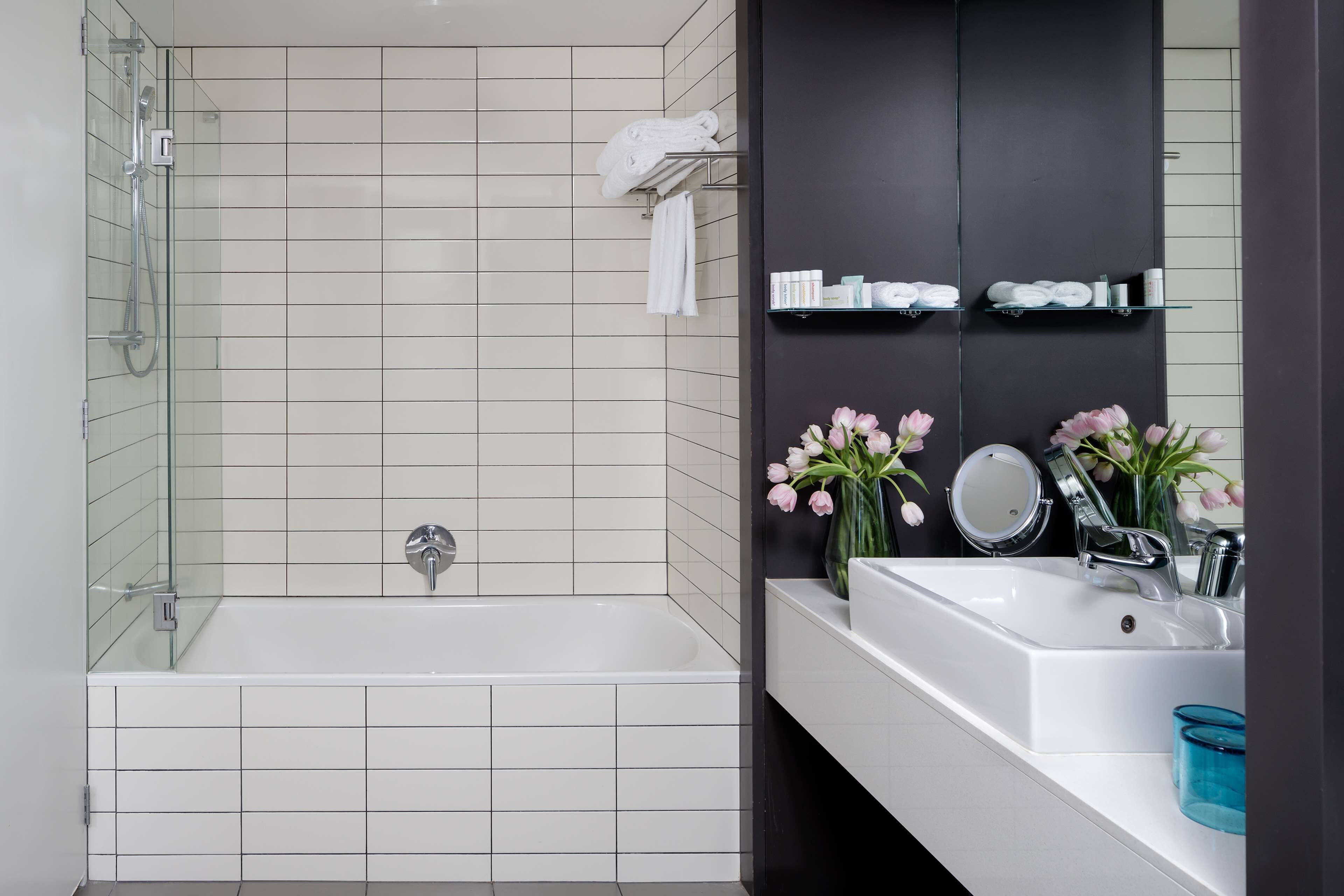 A modern bathroom with a bathtub, a sink, a mirror, and a vase of flowers.