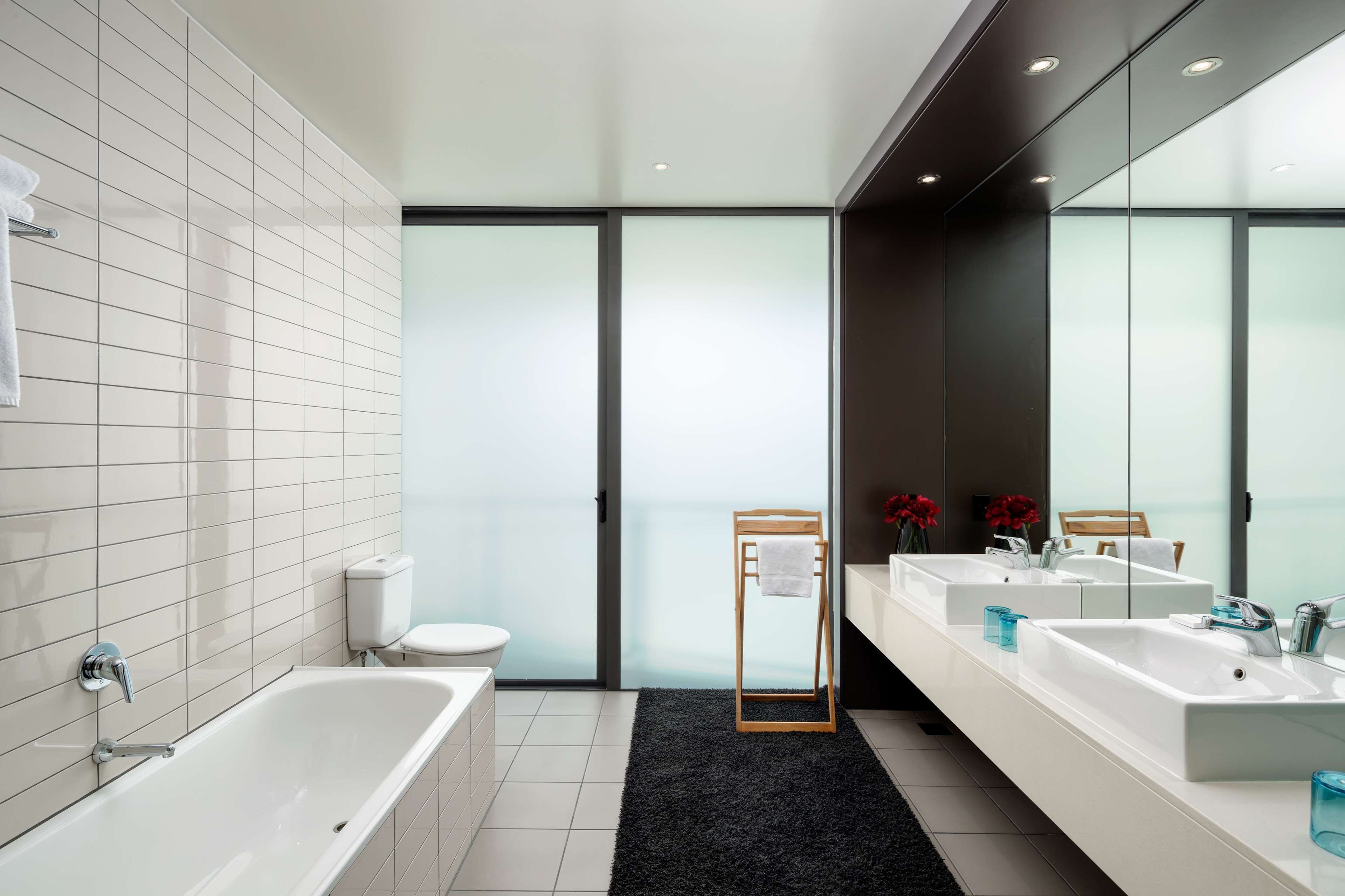 A modern bathroom with a bathtub, two sinks, a toilet, and a large mirror.