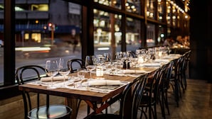 A restaurant with a long dining table set for a meal, large windows, and city lights visible outside. - Rydges Wellington (Wellington)