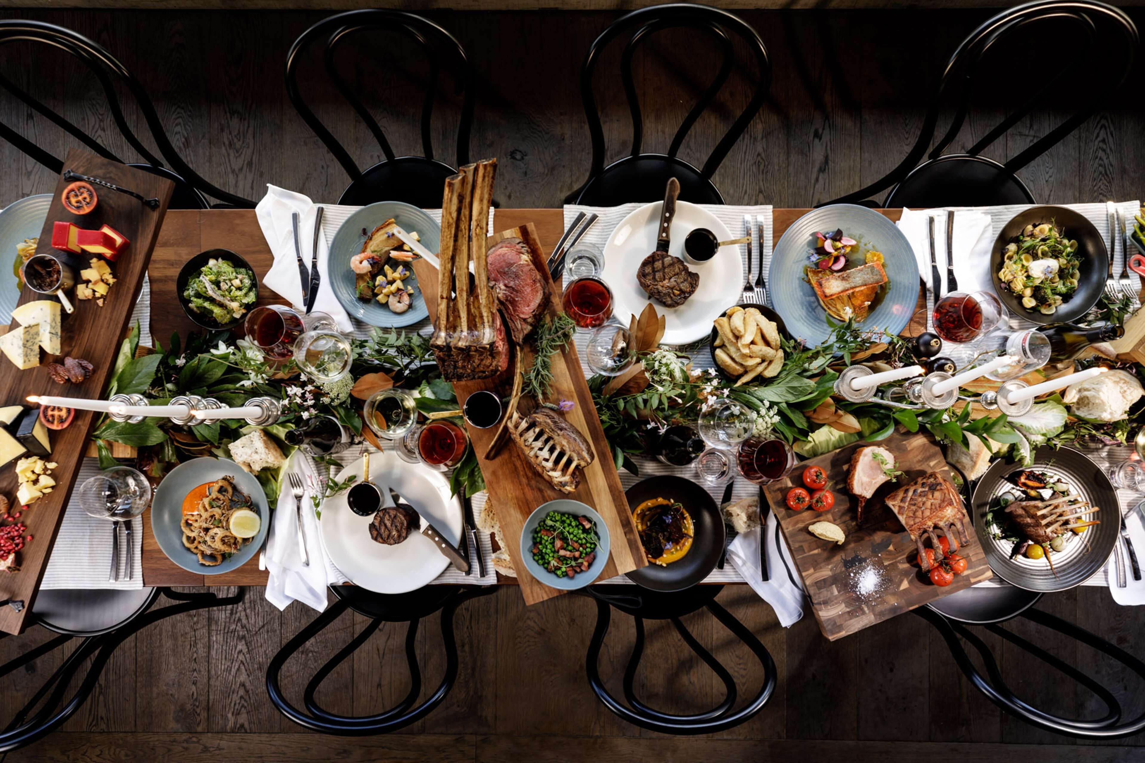A dining table set with various dishes, utensils, and glasses, surrounded by chairs.