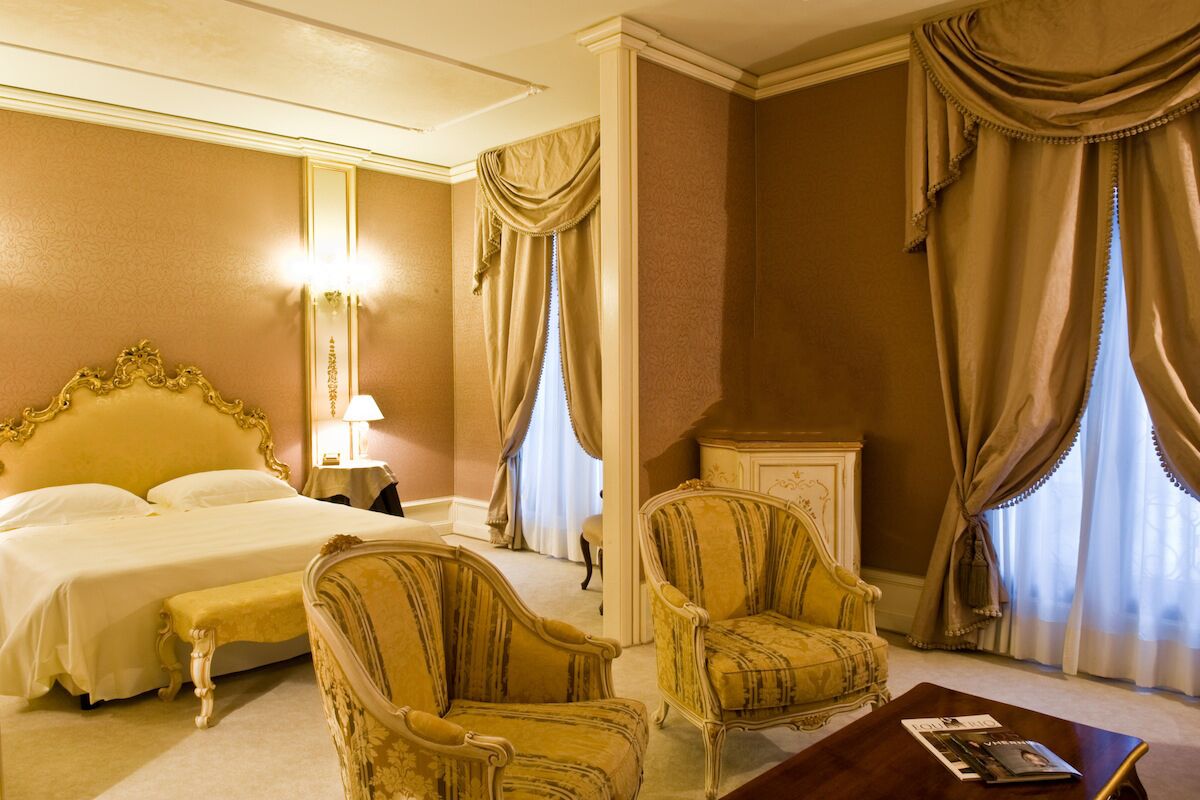 A hotel room with a large bed, two armchairs, a wooden coffee table, and a nightstand with a lamp.
