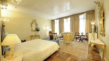 Une chambre d’hôtel dotée d’un grand lit, d’un coin salon avec un canapé et des fauteuils, d’une table à manger et d’un lustre.