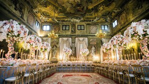 An ornate hall with a long table set for a formal event, flanked by floral arrangements and chandeliers. - Ca' Sagredo (Venice)