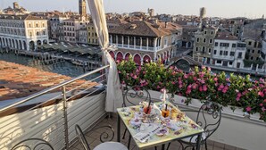 A balcony with a table set for two, overlooking a canal with historic buildings and a bridge. - Ca' Sagredo (Venice)