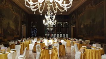 A banquet hall with round tables, white chairs, and a large chandelier.