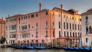 A historic building with multiple windows and balconies, a sign reading "C'EST S'AGREDO", and several gondolas docked in the water.