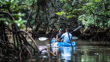 Two people kayaking on a calm river surrounded by dense foliage and rocky terrain.