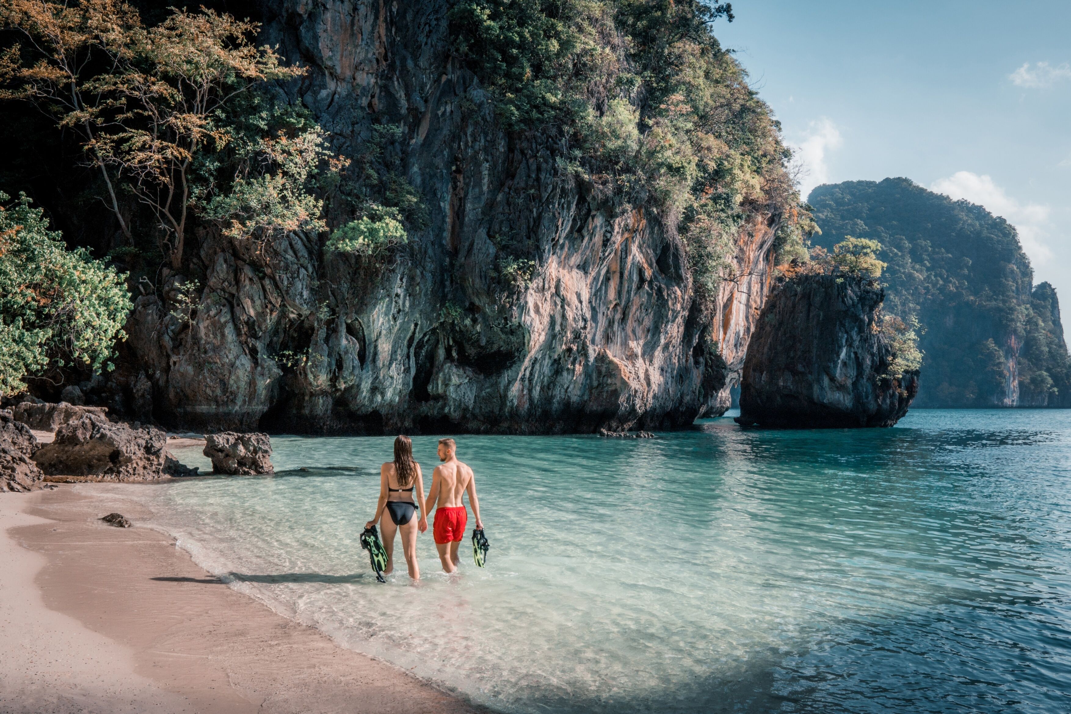 A beach with clear water and rocky cliffs.