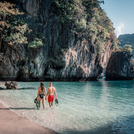 A beach with clear water and rocky cliffs.
