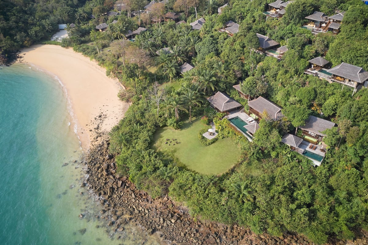 An aerial view of a coastal resort with multiple bungalow-style houses, a sandy beach, and lush greenery.