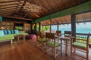 A spacious room with a wooden floor, a green sofa, wooden chairs, and a table.