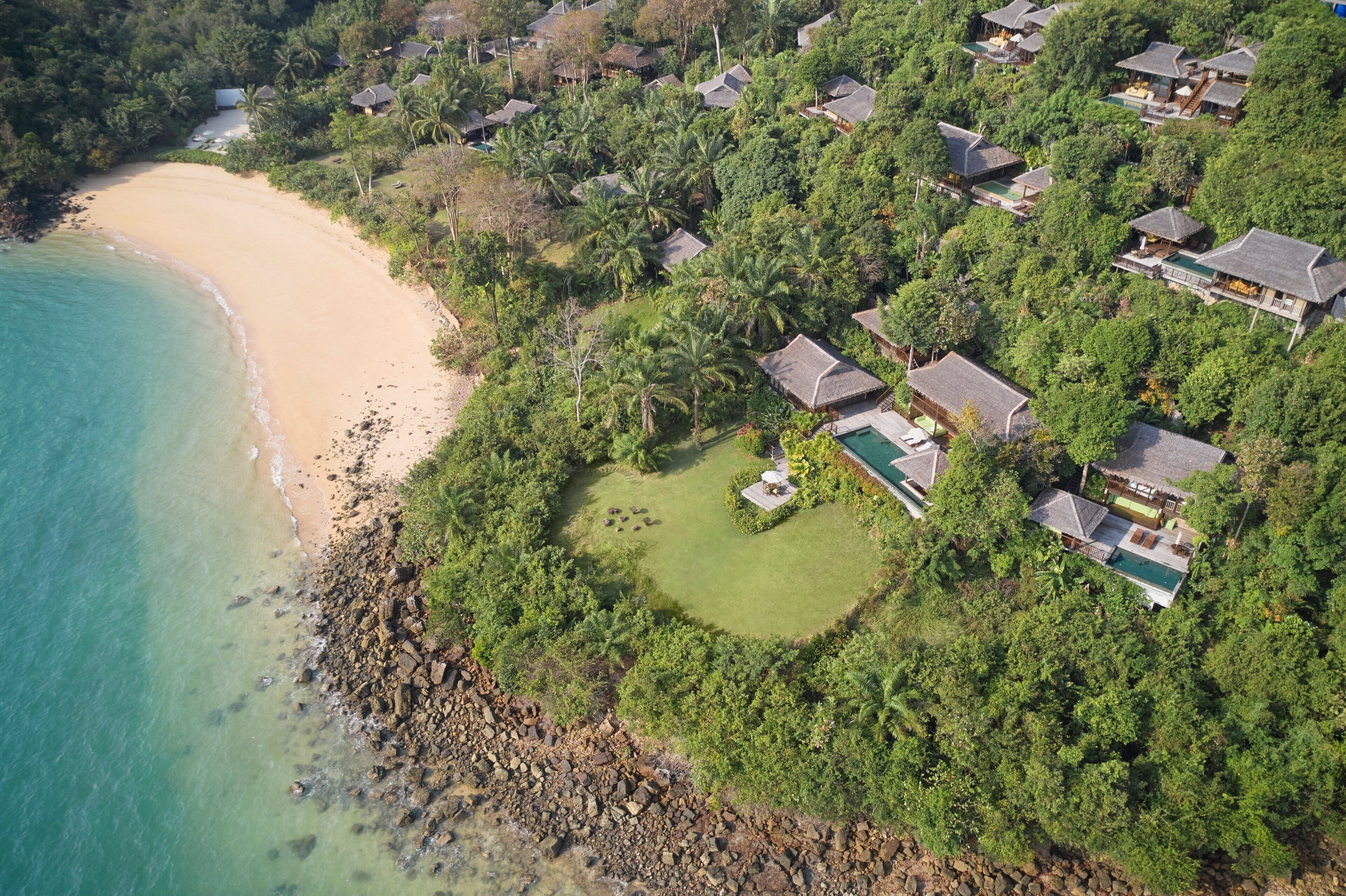 Ett flygbildsbild av en kustort med flera byggnader i bungalowstil, en sandstrand och en fri utsikt över havet.