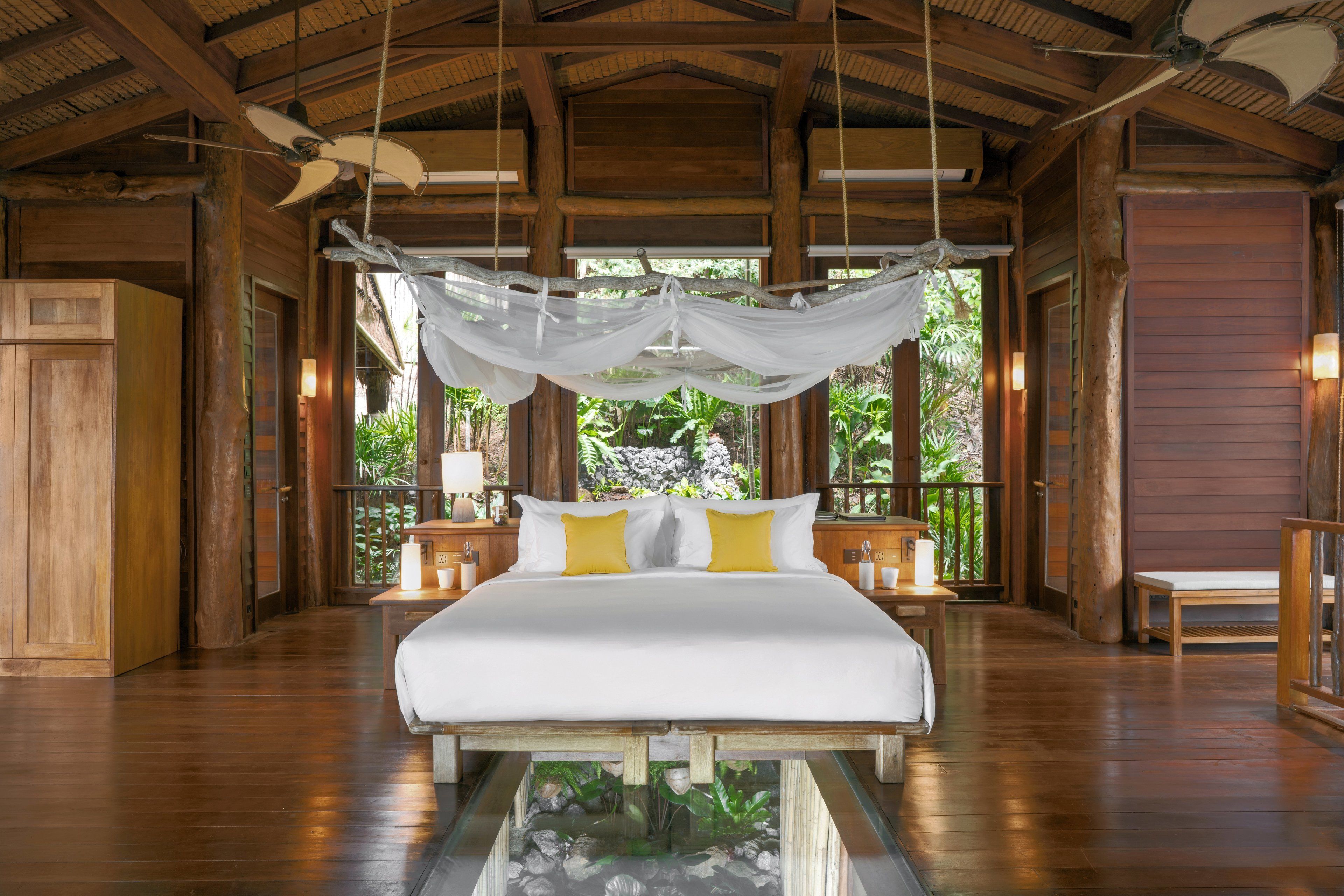 A spacious bedroom with a large bed, wooden walls, and a view of lush greenery.