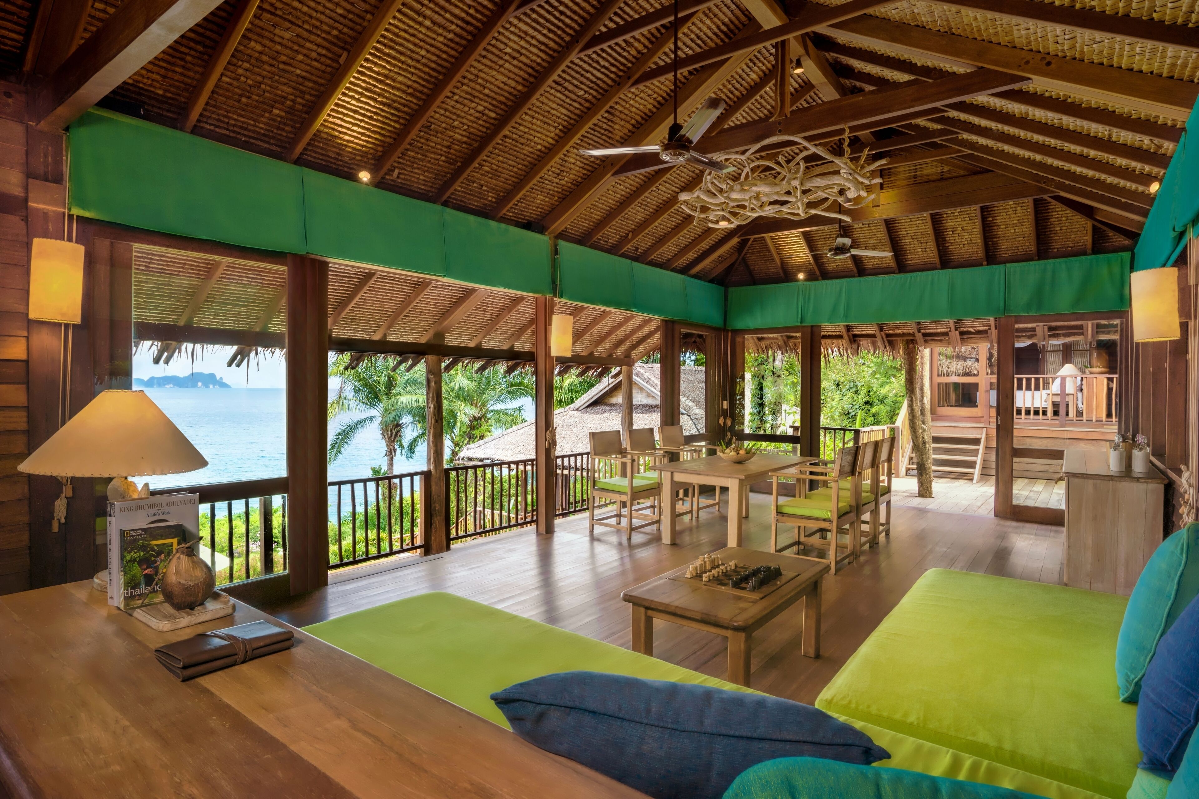 A spacious room with a wooden ceiling, a green sofa, a wooden table, and a view of the ocean.