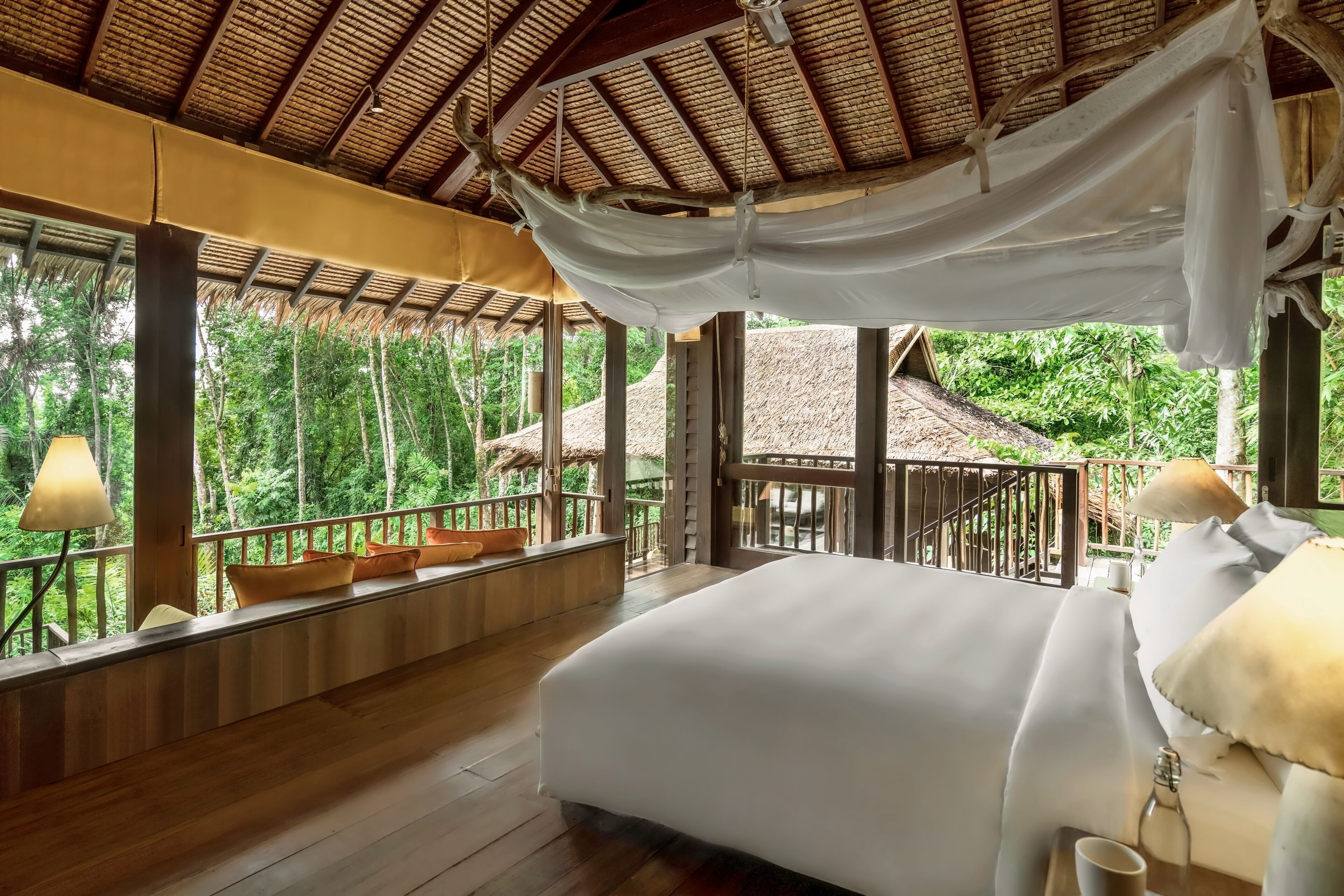 A room with a bed, wooden floor, windows, and a balcony with cushions.
