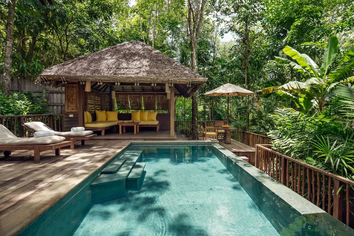 A pool area with wooden deck, lounge chairs, and a thatched-roof structure.