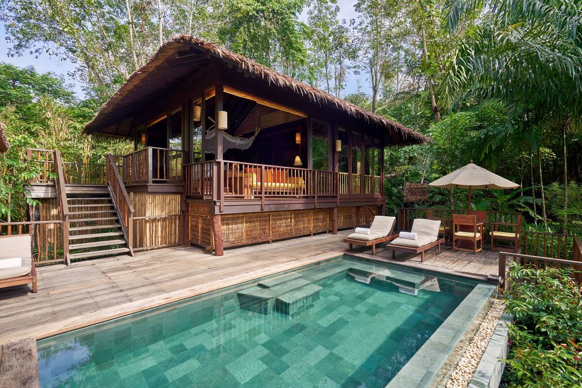 A wooden deck with a pool, lounge chairs, and a thatched-roof structure.