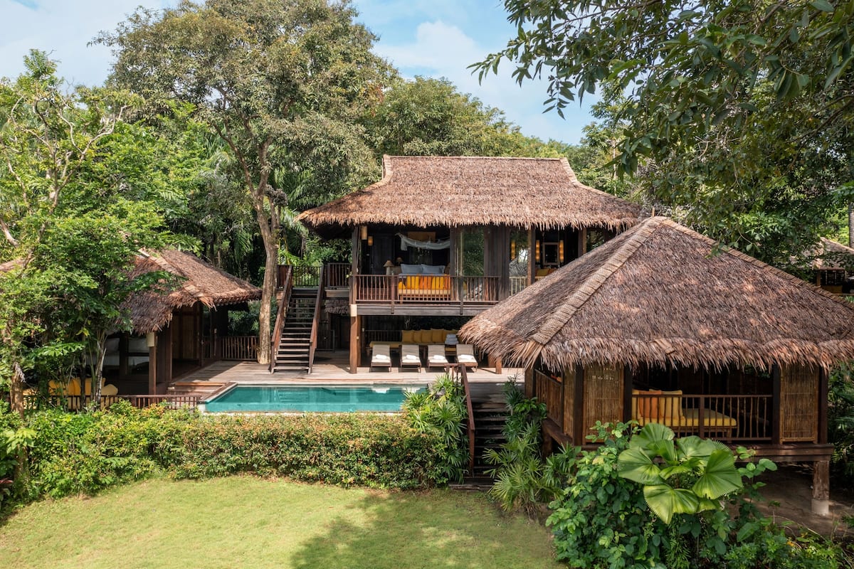 A resort with multiple thatched-roof structures, a central pool, and lush greenery.