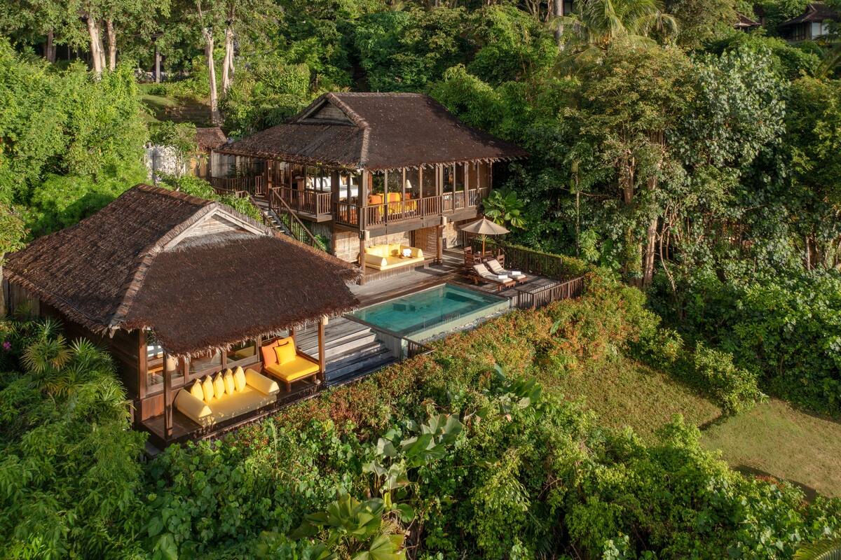 A two-story wooden house with a pool, surrounded by dense greenery.