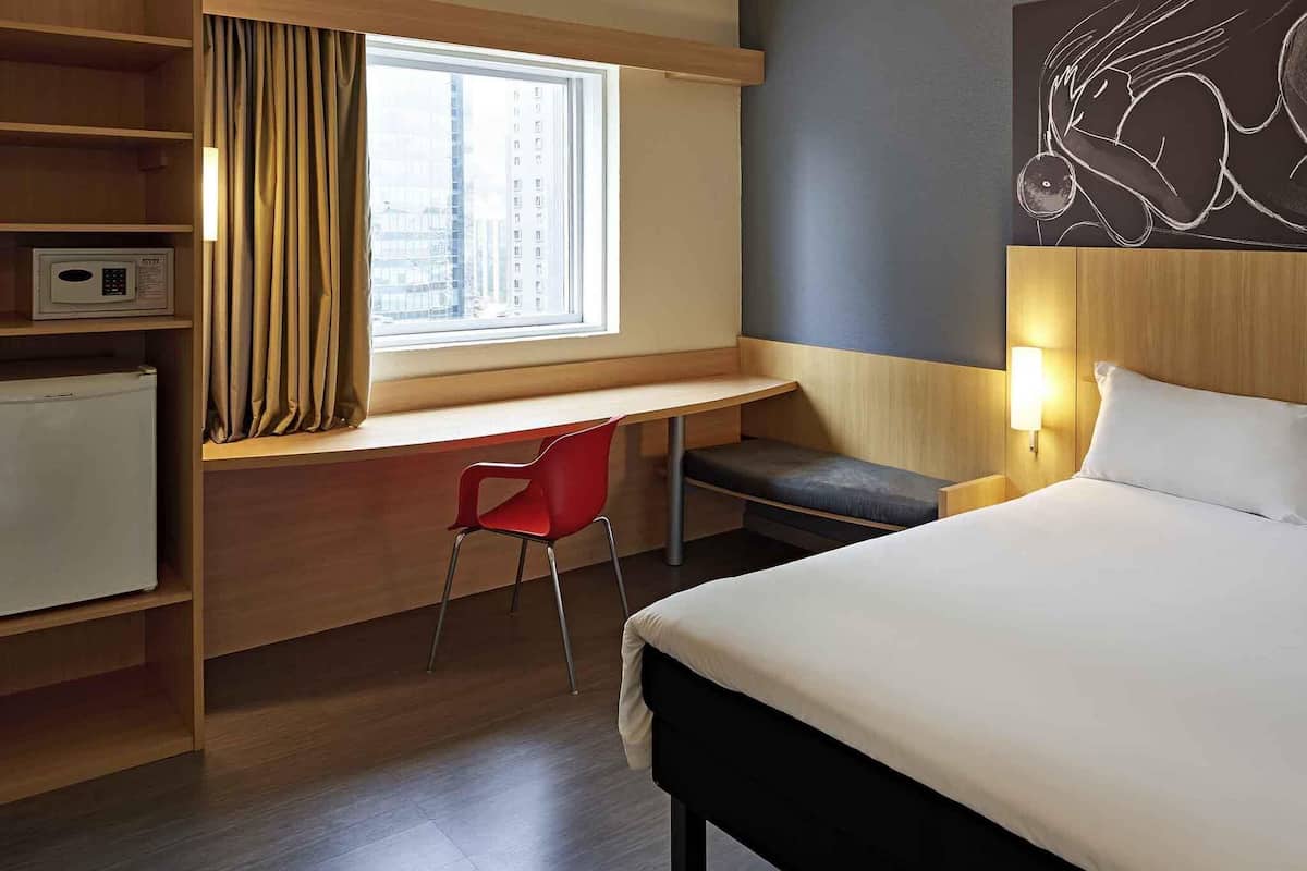 A hotel room with a bed, a desk, a chair, a microwave, and a window with curtains.