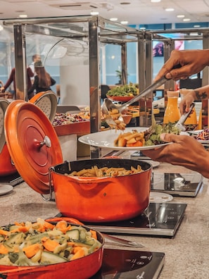 Montaje de bufé con diversas opciones de comida, como pasta, ensaladas y un recipiente con comida caliente.