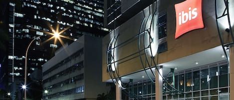 A modern building with a prominent 'ibis' sign, large windows, and a yellow taxi parked in front.