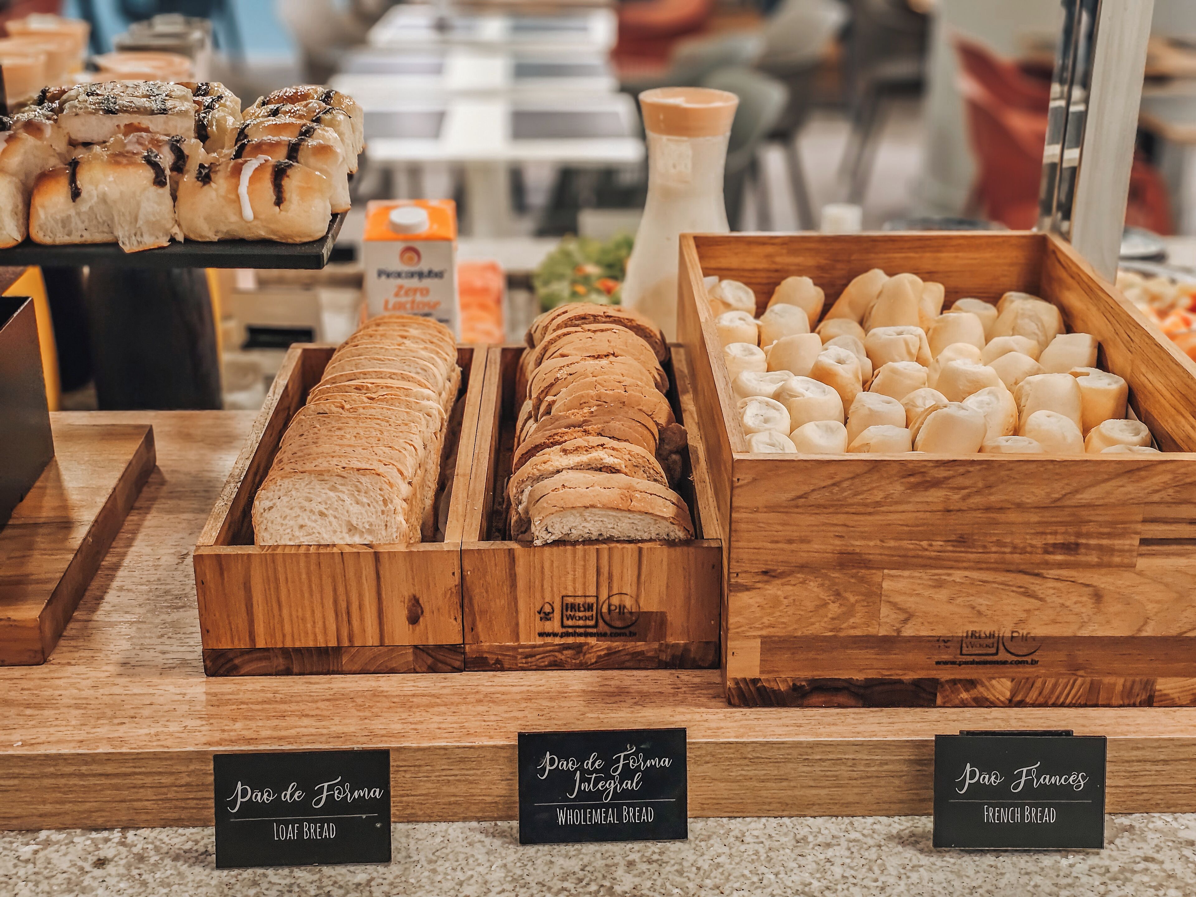 Una vitrina de panadería con varios tipos de pan, incluyendo pan integral y baguette, con etiquetas para facilitar la identificación.