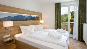 Hotelkamer met een groot bed, een houten hoofdbord, een nachtkastje, een lamp en uitzicht op bergen door een raam.