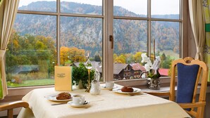 Een eettafel met uitzicht op herfstbomen en bergen door grote ramen.