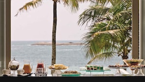 A breakfast table with various dishes and drinks, overlooking a beach with palm trees and the ocean. - Hotel Jequitimar Guarujá Resort & Spa by Accor (Guarujá)