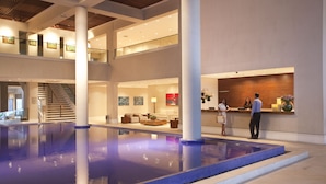 A spacious indoor pool area with a clear view of the reception desk and a staircase leading to upper levels. - Hotel Jequitimar Guarujá Resort & Spa by Accor (Guarujá)
