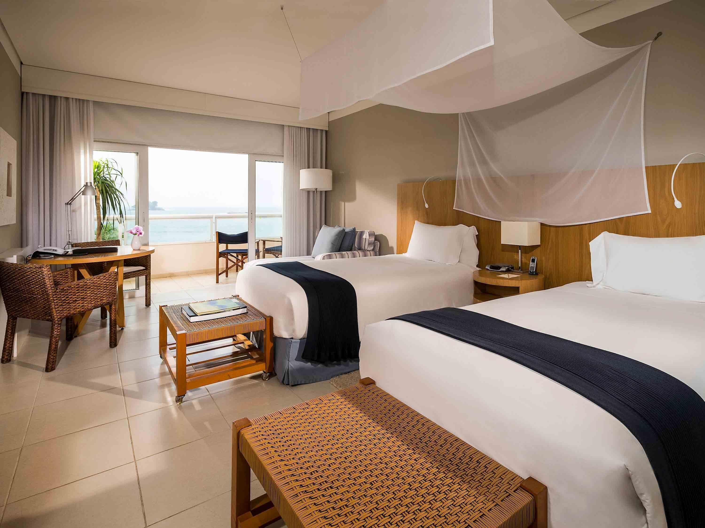 Une chambre d’hôtel avec deux lits, un balcon, un coin repas et une vue sur la mer.