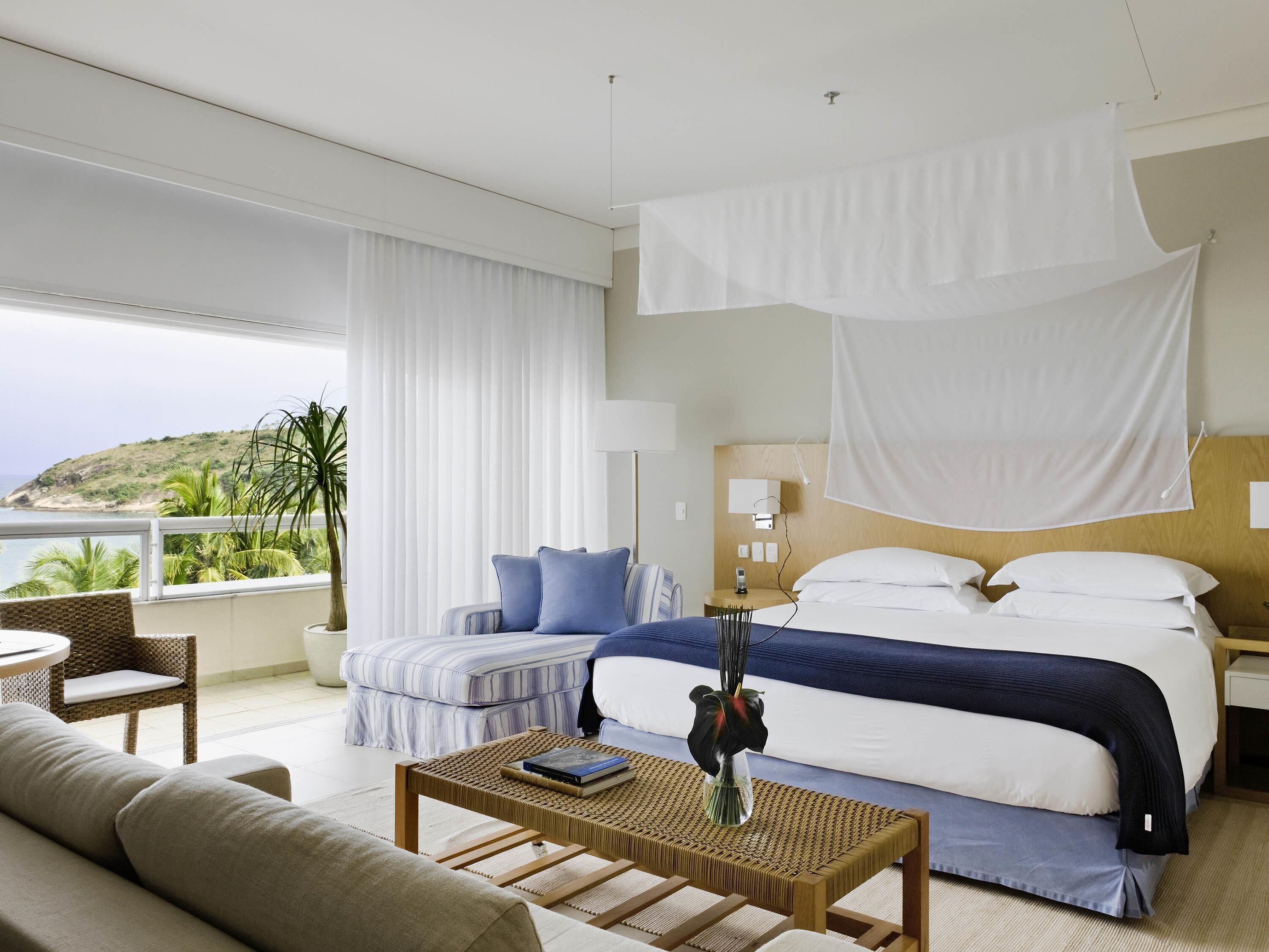 Une chambre d’hôtel avec un lit, un canapé, une petite table, une table de chevet et une vue sur l’océan.
