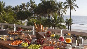 A buffet table with various fruits, pastries, and beverages on a wooden deck overlooking the ocean. - Hotel Jequitimar Guarujá Resort & Spa by Accor (Guarujá)