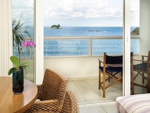 Ein Balkon mit einem Korbstuhl, einem kleinen Tisch mit Blumenvase und Blick aufs Meer.