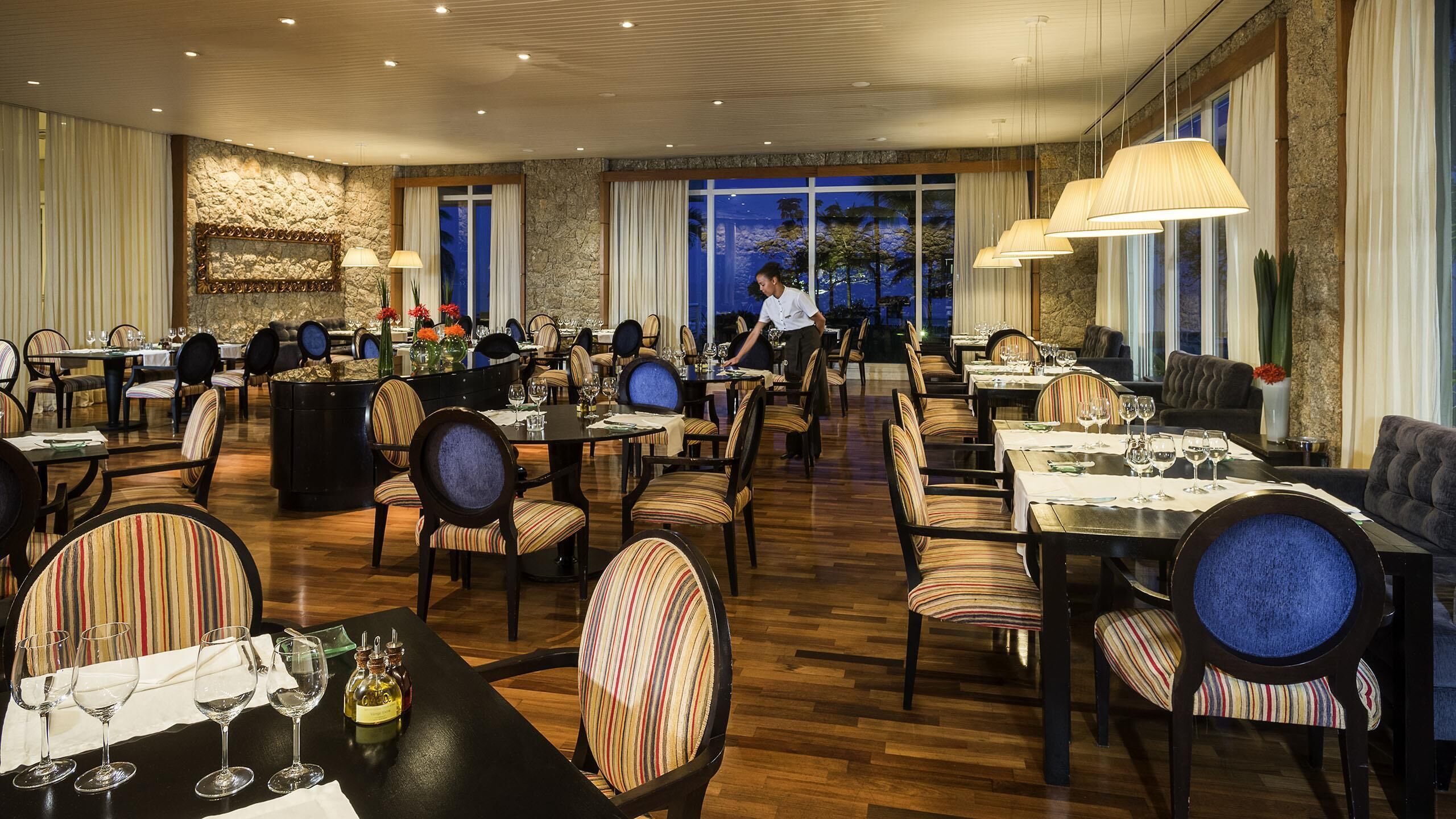 Ein Restaurant mit mehreren Tischen, Stühlen und einem Kellner.
